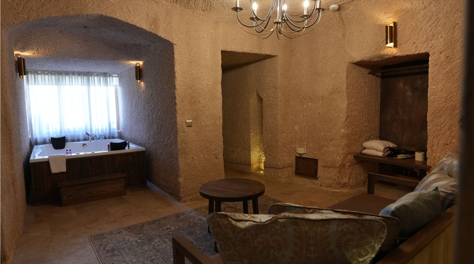 Una habitación acogedora con pared de piedra, un banco de madera, una mesa redonda y un sofá.