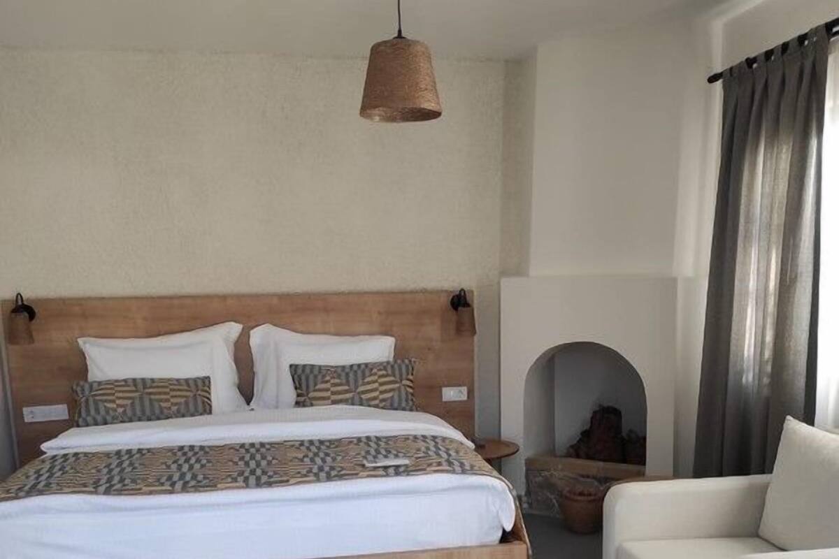 A bedroom with a wooden bed, a white sofa, a hanging light fixture, and a fireplace.