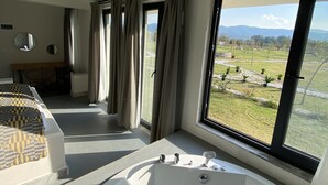 A bedroom with a large window, a bathtub, and a bed with patterned bedding. - ALBIZIA BOUTIQUE HOTEL (Ula)