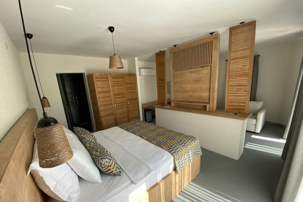 A bedroom with a bed, wooden headboard, hanging light, and built-in wardrobe.