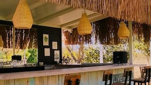 A bar area with a thatched roof, hanging wicker lamps, and wooden bar stools. - ALBIZIA BOUTIQUE HOTEL (Ula)