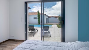 A bedroom with a large sliding glass door leading to a patio with a pool and lounge chairs.
