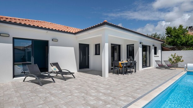 A modern house with a swimming pool, a patio with lounge chairs, and a dining area.