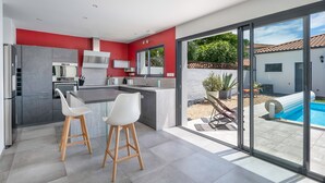 A modern kitchen with a red accent wall, a large island with bar stools, and a sliding glass door leading to a pool area.