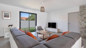 A modern living room with a grey sofa, a coffee table, a TV, and a large window with a view of greenery.