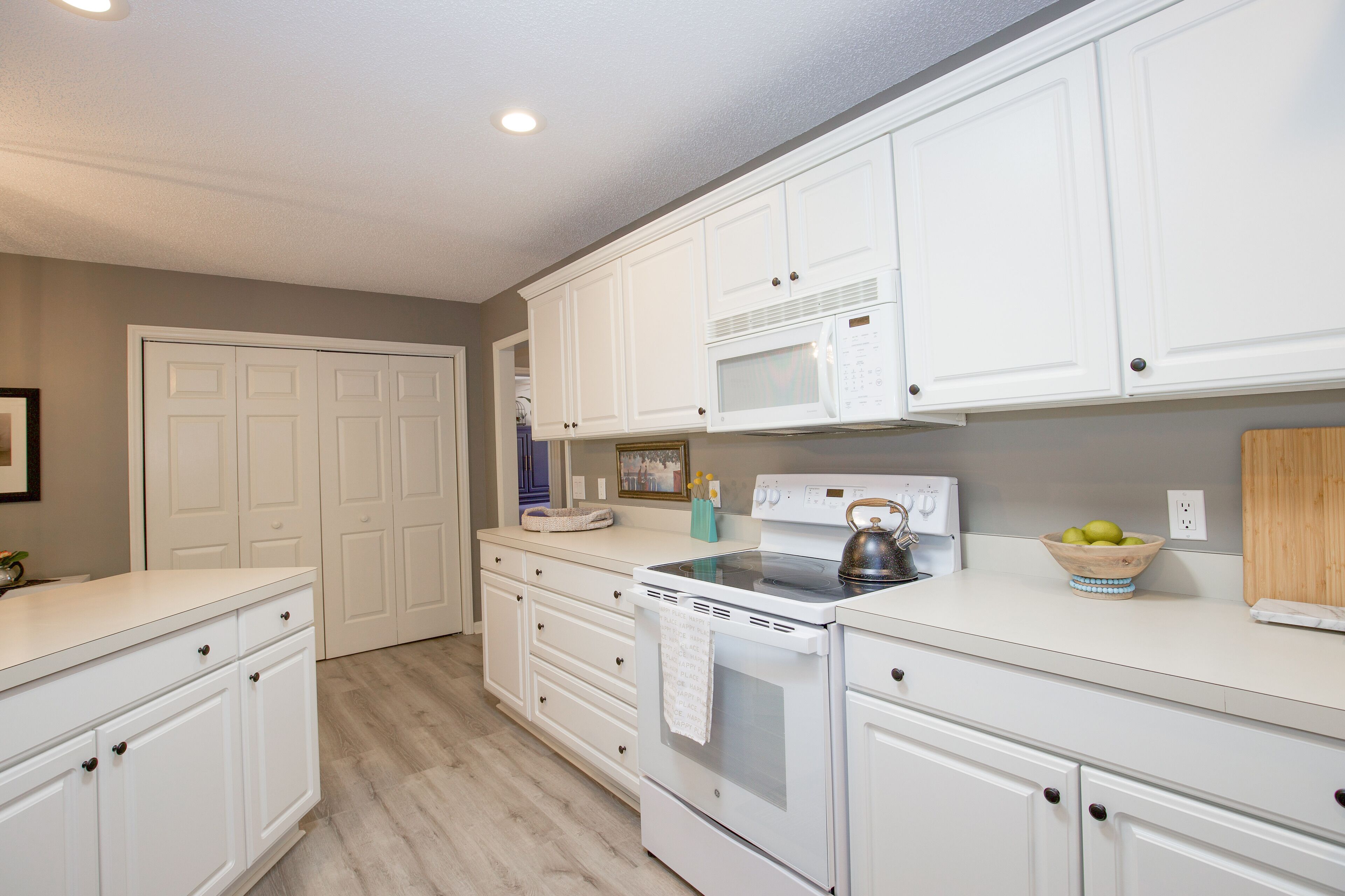 A kitchen with white cabinetry, a stove, a microwave, and a bowl of fruit on the counter.