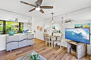 A modern living room with a wooden floor, a dining area, and a large TV displaying a wave.