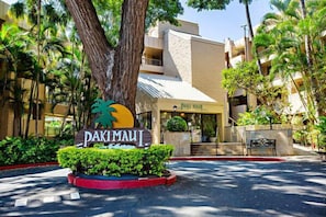 A hotel entrance with a sign reading "PAKIMAUI," surrounded by lush greenery and palm trees.