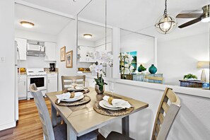 Une cuisine moderne avec des meubles blancs, un four à micro-ondes et une cuisinière. On y trouve une table à manger dressée avec des assiettes, des couverts et un vase rempli de fleurs.