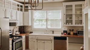A kitchen with white cabinets, a stainless steel refrigerator, a built-in oven, a microwave, and a window with blinds. - The Yellow House - Hidden Gem in heart of Portland (Portland)