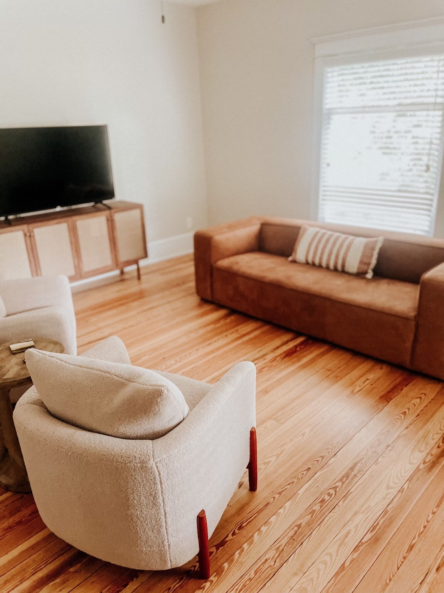 Ein Wohnzimmer mit einem beigefarbenen Sessel, einem braunen Sofa, einem Holzschrank und einem Fernseher.