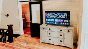A living room with a flat-screen TV mounted on a cabinet, a wooden staircase, and a door leading to another room. - The Yellow House - Hidden Gem in heart of Portland (Portland)