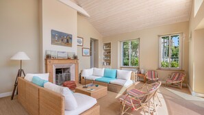 A spacious living room with wicker furniture, a fireplace, and large windows offering natural light.