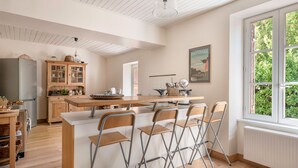 A modern kitchen with wooden cabinets, a central island with bar stools, and a large window with a view of greenery.