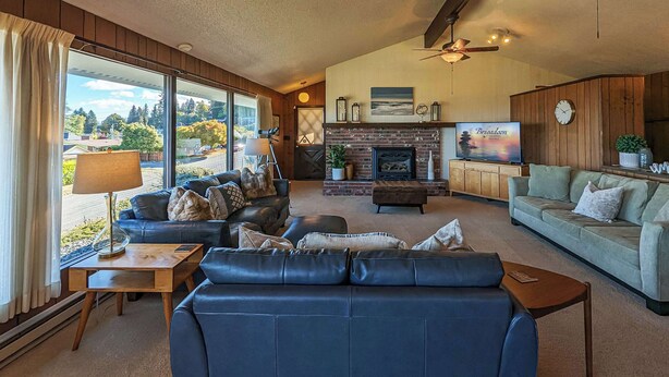 A spacious living room with a fireplace, leather sofas, and a television. - Panoramic Water Views, Retro Vibe, EV Charger, (Port Angeles)