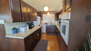 A compact kitchen with wooden cabinets, a countertop with a coffee maker, toaster, and a potted plant. - Panoramic Water Views, Retro Vibe, EV Charger, (Port Angeles)