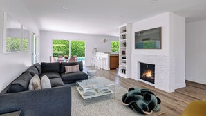Una sala de estar moderna con chimenea, un sofá, una mesa de centro y vistas a una piscina y zona exterior.