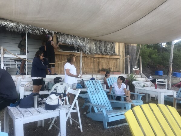 Outdoor seating with chairs and tables, a thatched roof, and a wooden structure in the background.