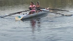 Ein Ruderboot auf ruhigem Wasser, im Hintergrund ein bewaldeter Hügel.