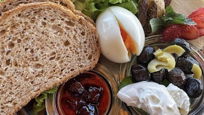 Ein Teller mit Gurkenscheiben, Salat, einer halbierten gekochten Eiers, Erdbeeren, schwarzen Oliven und einer Schale rote Marmelade und weiße Sahne.