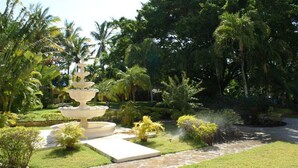 Une fontaine à plusieurs niveaux, entourée d’une végétation luxuriante et de palmiers.