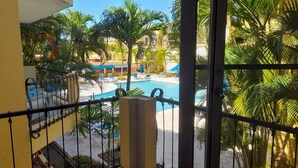 Un balcon donnant sur une piscine, entourée de palmiers et de chaises longues.
