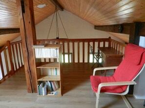 Quarto em estilo loft com teto de madeira, uma estante de madeira, uma cadeira vermelha e uma escrivaninha de madeira.