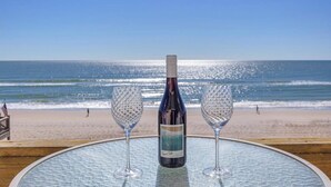 Een tafel met een fles wijn en twee glazen op een strand met uitzicht op de oceaan.