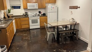 A kitchen with wooden cabinets, a white stove, a microwave, a refrigerator, and a dining table with chairs. - Cozy 2 Bed (Sterling)