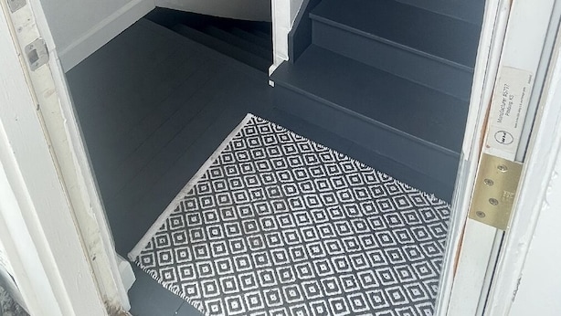 A staircase with a black handrail and a patterned rug at the bottom. - Cozy 2 Bed (Sterling)