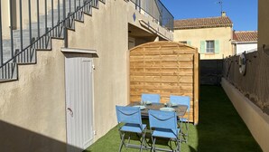 Een binnenplaats met een tafel, stoelen, een houten poort en een trap naar een hoger gelegen niveau.