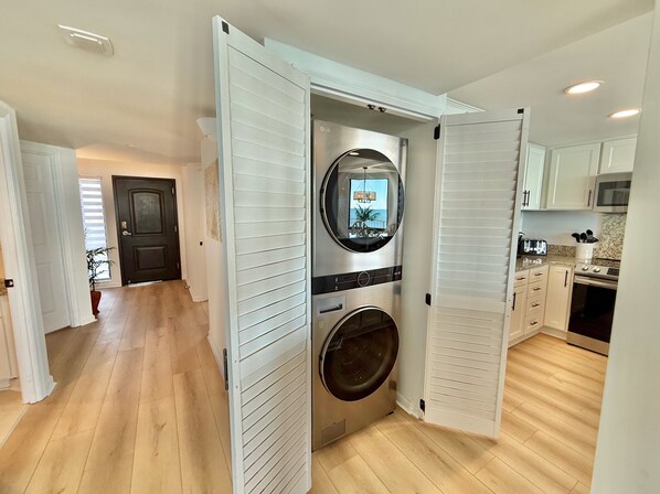 A compact kitchen with a built-in washer and dryer, white cabinetry, and a view of the living area through an open door. - Spectacular, spacious, renovated corner unit #501 with large wrap around balcony (Garden City)