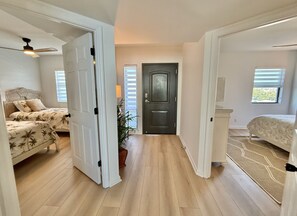 Un hall d’entrée spacieux, avec un lit sur la gauche, une porte au fond et une fenêtre sur la droite.