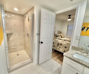 Une salle de bain moderne avec une douche à parois de verre, une porte blanche, un lit recouvert d ’une couvre-lit à motifs floraux et un meuble-lavabo.