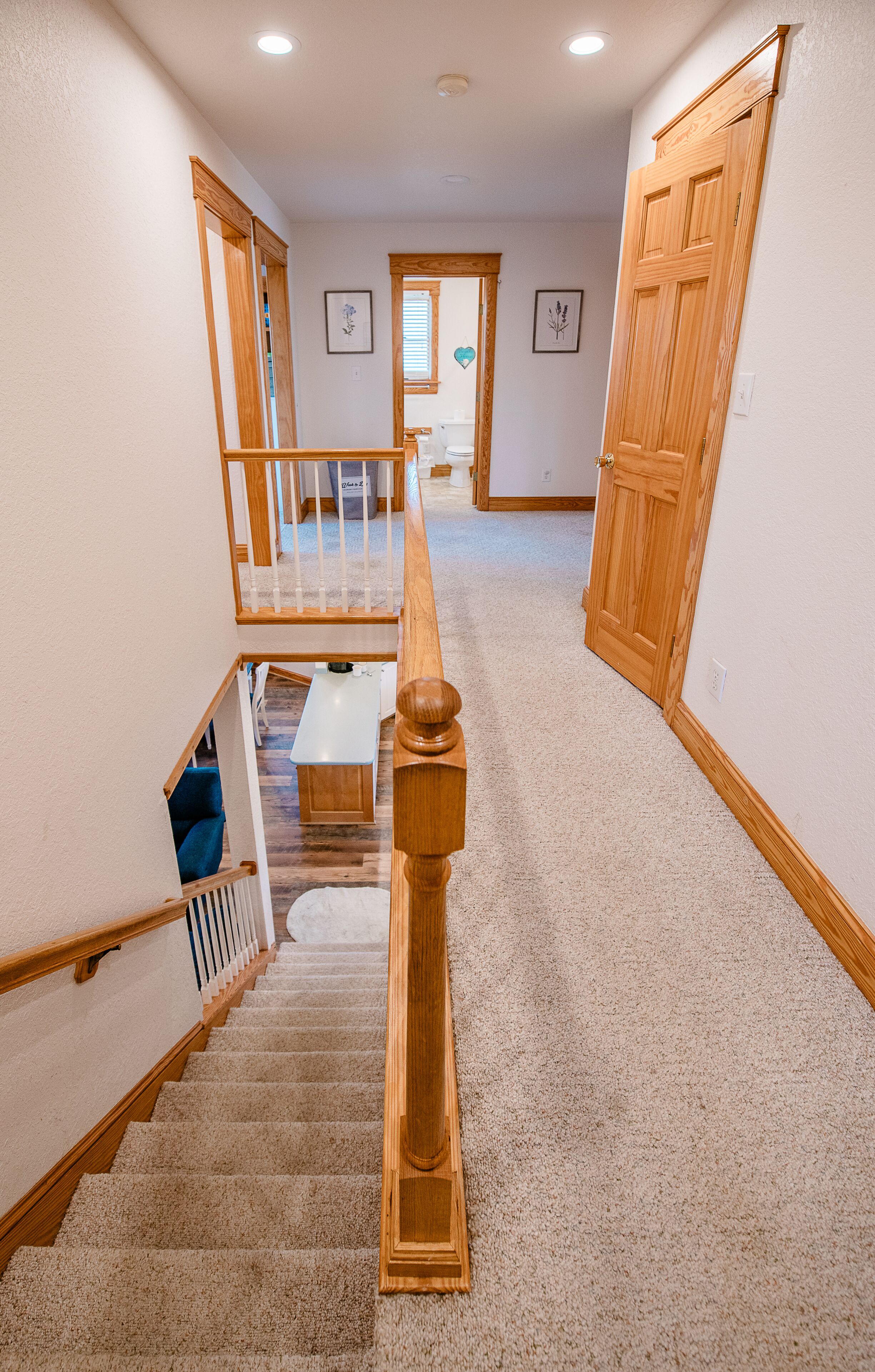 A carpeted staircase with wooden railings and a handrail, leading to a second-floor landing with a bench and a door.