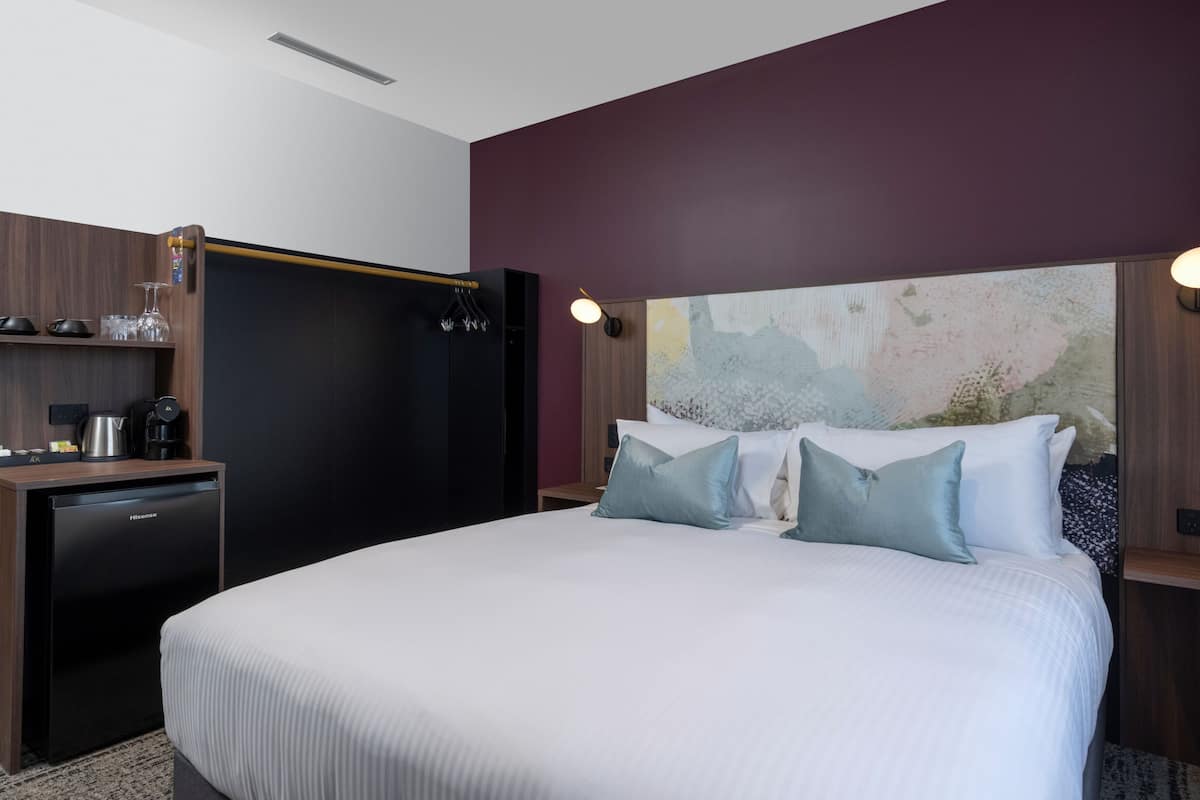 A hotel room with a bed, a desk with a coffee maker, and a wall-mounted TV.