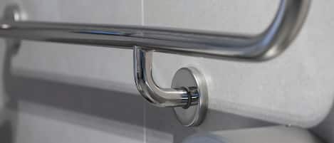 A bathroom with a chrome handrail and a round, metallic faucet.