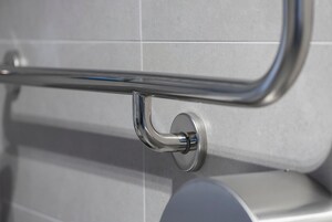 A bathroom with a chrome handrail and a round, metallic faucet.