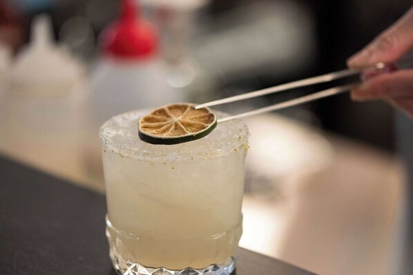 A cocktail with a lime garnish being held by tongs.