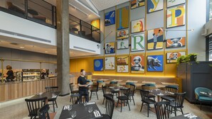 Un ristorante moderno con diversi tavoli e sedie, un bancone con teca espositiva e diverse opere d'arte colorate alle pareti.