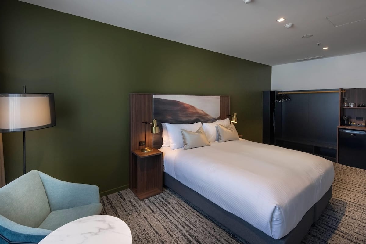 A modern hotel room with a large bed, a flat-screen TV, a desk, and a lamp.