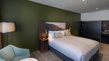 A modern hotel room with a large bed, a flat-screen TV, a desk, and a lamp.