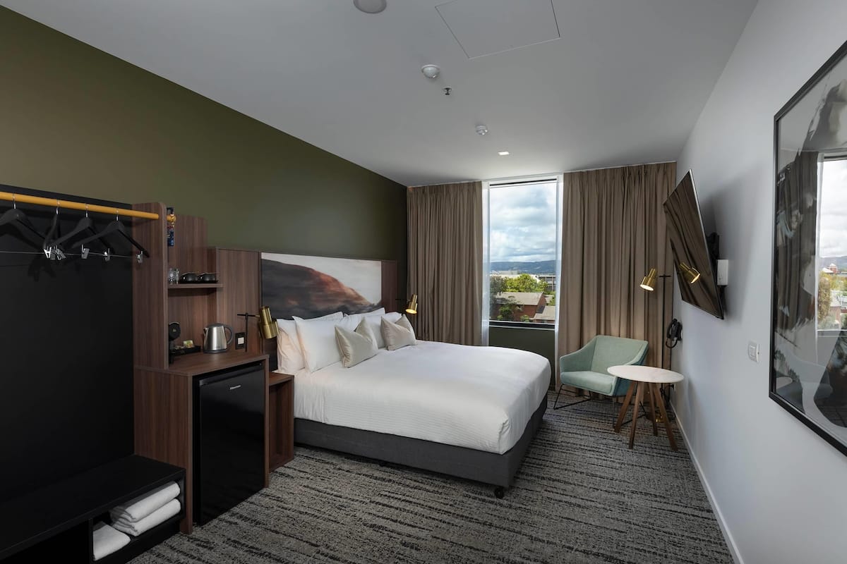 A modern hotel room with a large bed, a desk with a computer, a small table, and a view of the outdoors.