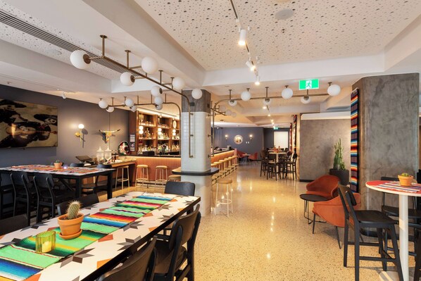 A modern bar area with a long counter, stools, and a variety of bottles and glasses. - Tryp Adelaide by Wyndham (Adelaide)