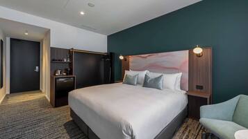 Une chambre d’hôtel avec un grand lit, un bureau avec une chaise, une armoire et une table de chevet avec une lampe.