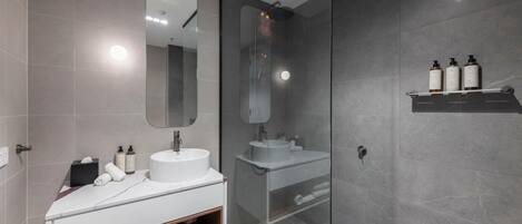 A modern bathroom with a glass-enclosed shower, a white vanity with a mirror, and a shelf with toiletries.