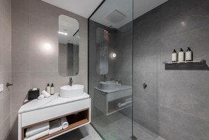 Un baño moderno con ducha de vidrio, tocador blanco con espejo y repisa con artículos de aseo.