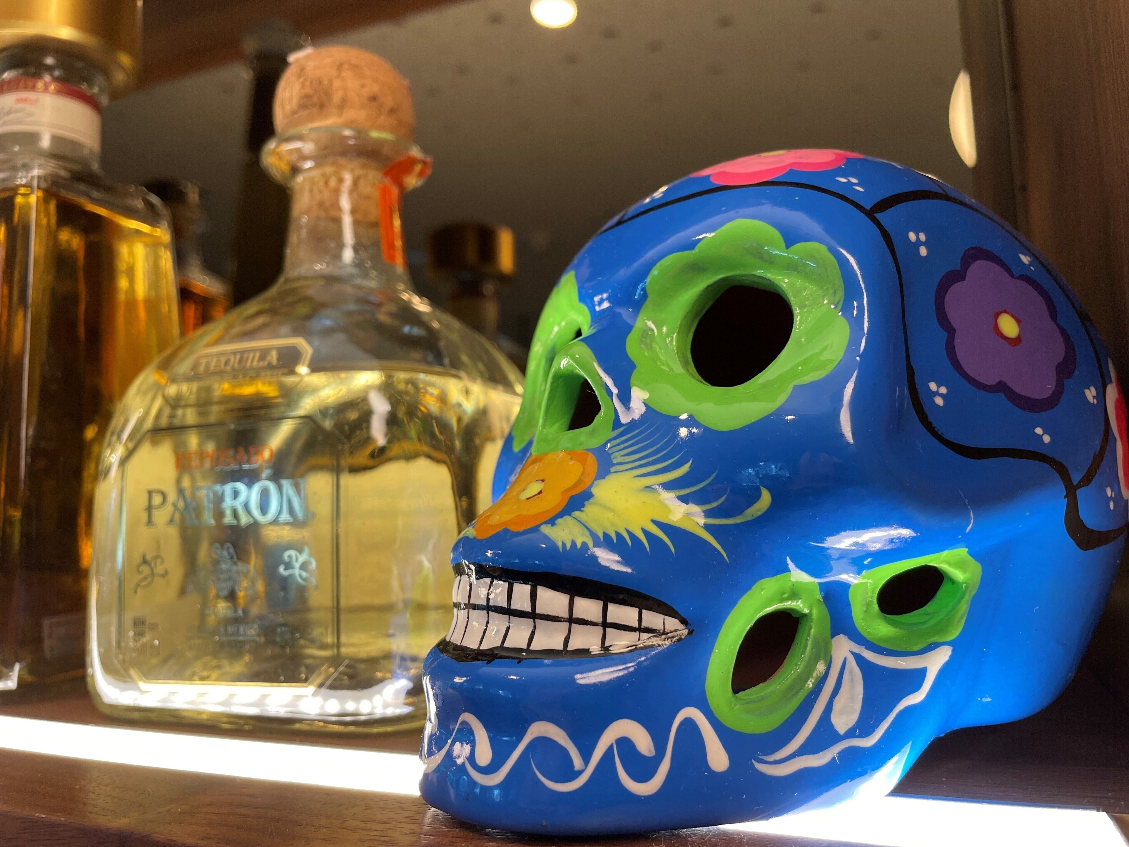 Un crâne aux couleurs vives et une bouteille de tequila Patron sont posés sur une étagère.