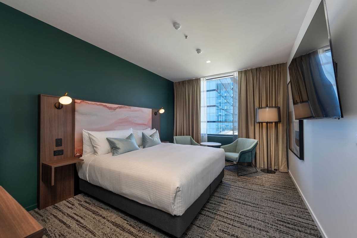 A modern hotel room with a large bed, a desk, a chair, and a TV.