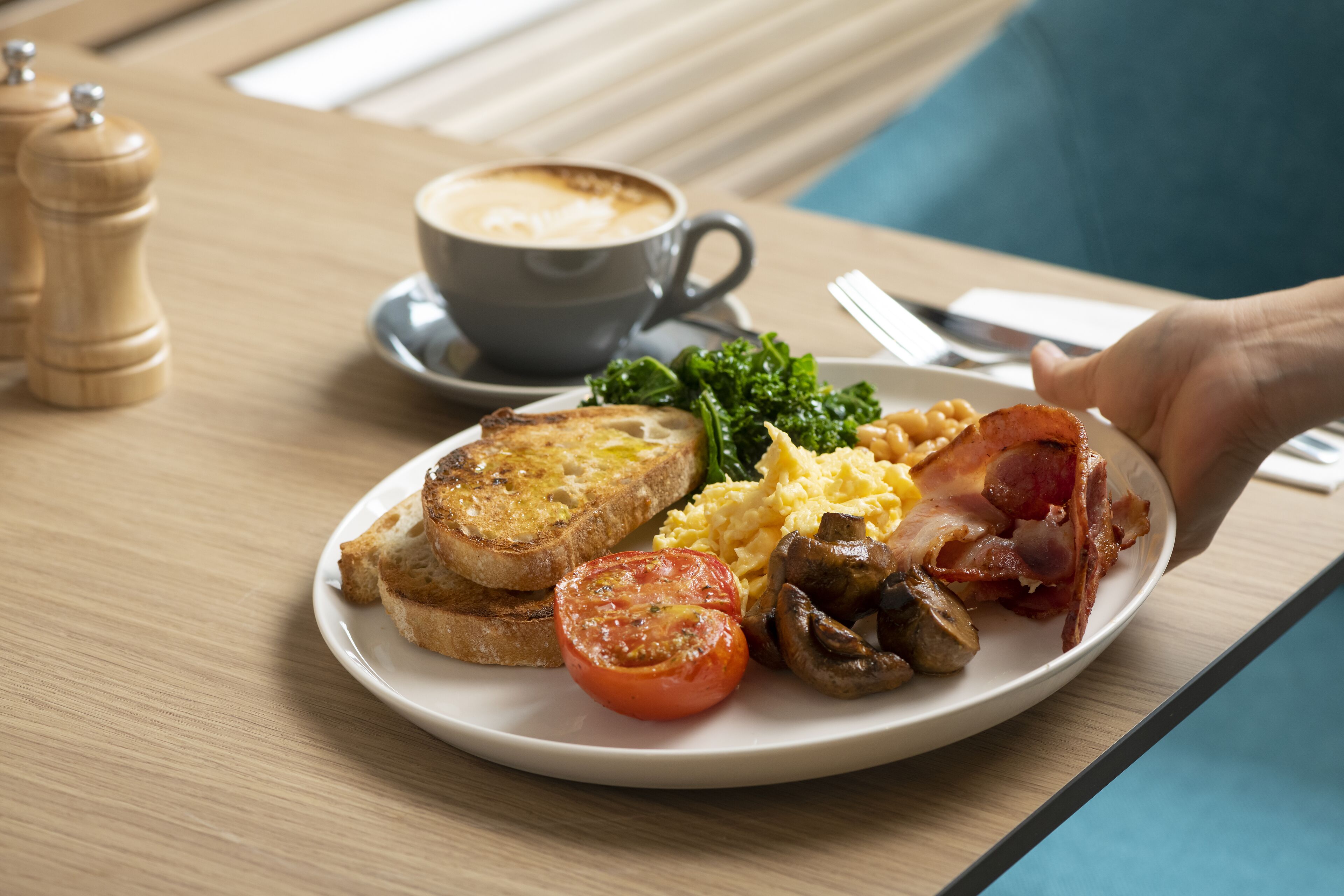 A plate of breakfast food including toast, scrambled eggs, bacon, mushrooms, spinach, and a tomato slice.